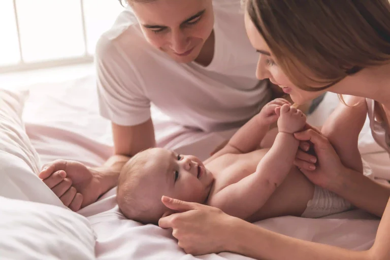 Nybakte foreldre smiler og leker med det nyfødte barnet på sengen.